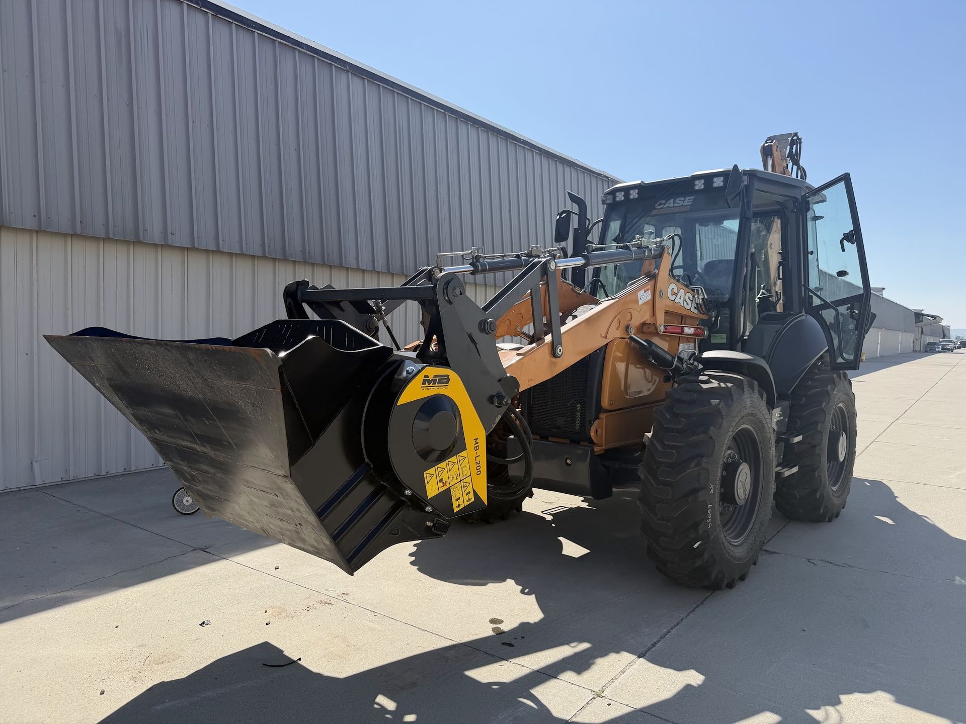 Backhoe loader with a front bucket parked beside a warehouse | American Jet Center